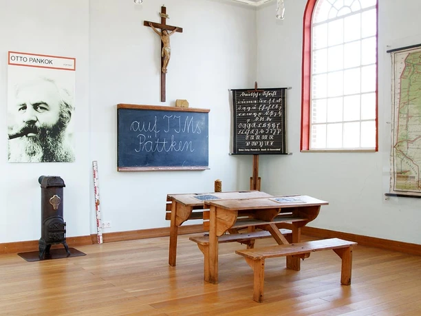 Alte Schule Bokeloh Historisches Klassenzimmer mit Holzbänken, Tafel, Landkarte und Kreuz in der Alten Schule Bokeloh.