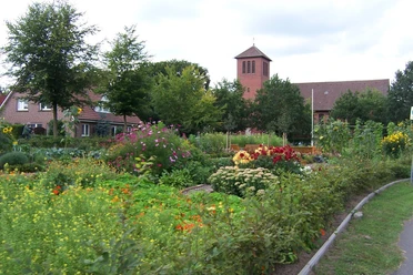 Bauerngarten Rühle Bauerngarten mit bunten Blumenbeeten, grünen Sträuchern und Blick auf Kirche und Backsteinhäuser