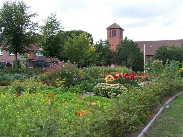 Bauerngarten Rühle Bauerngarten mit bunten Blumenbeeten, grünen Sträuchern und Blick auf Kirche und Backsteinhäuser