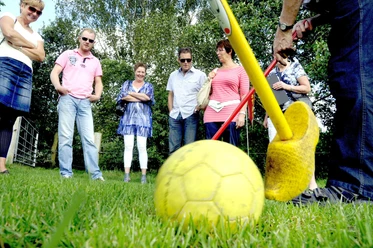 Bauerngolf Haren Gruppe Erwachsener spielt Bauerngolf auf einer Wiese, ein gelber Ball liegt vor einem Holzschläger.