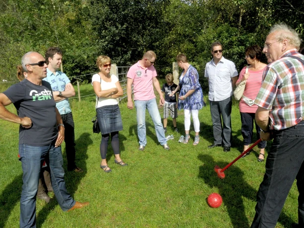 Bauerngolf Haren Gruppe von Menschen spielt Bauerngolf auf einer Wiese, ein Mann schlägt mit Holzschläger einen Ball.