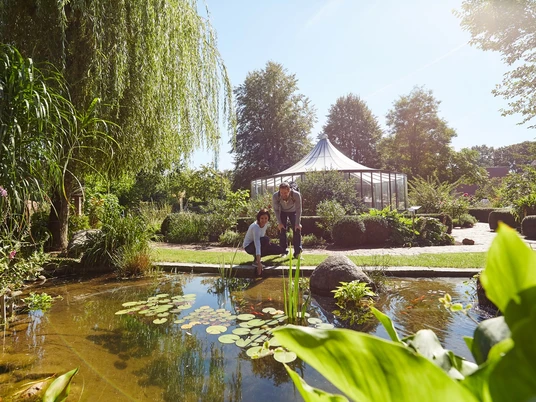 Bibelgarten Werlte Zwei Personen betrachten einen Teich mit Seerosen im grünen Bibelgarten Werlte bei Sonnenschein.