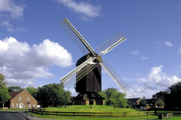 Bockwindmühle Papenburg Historische Bockwindmühle in Papenburg mit weißen Flügeln vor blauem Himmel und grüner Wiese.