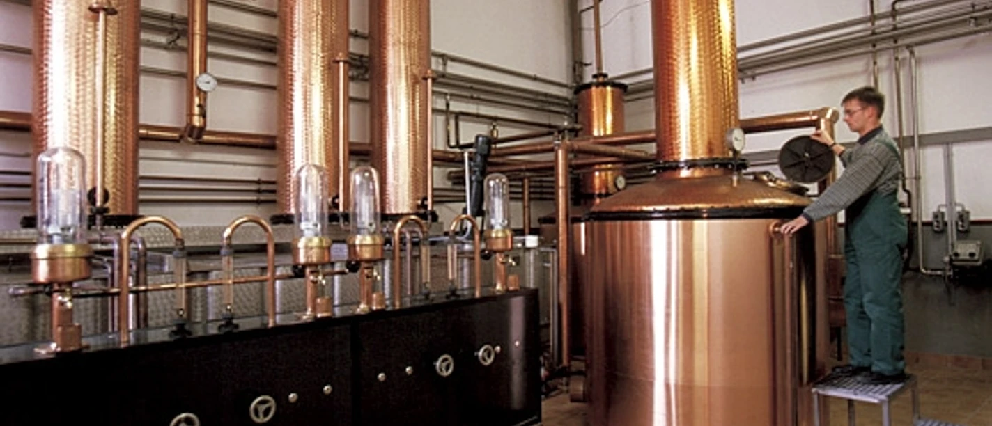 Brennereimuseum Haselünne Kupferne Brennblasen und Rohrleitungen mit Arbeiter in grünem Overall in einer historischen Destille.