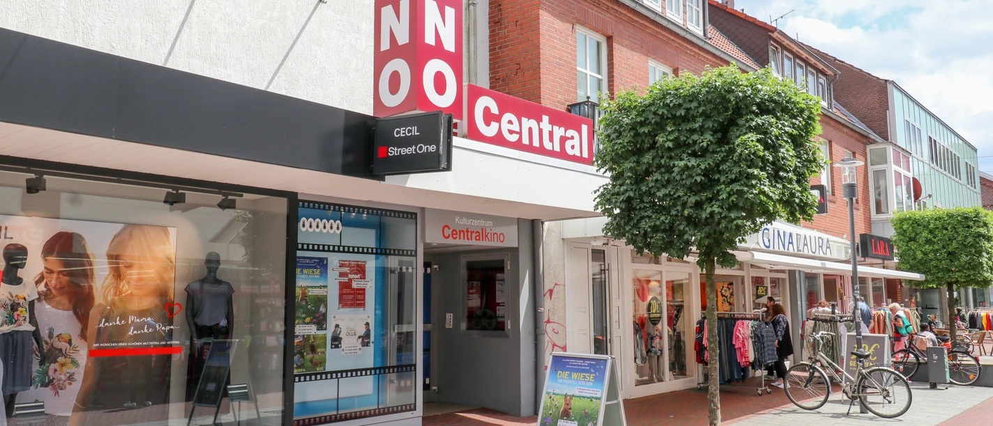 Eingang des Centralkino Lingen in einer Einkaufsstraße mit Geschäften, Plakatständer und Fahrrädern.