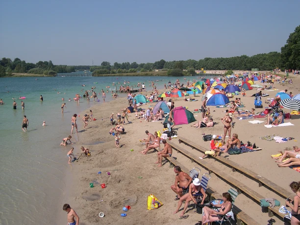 dankernsee-strand-6 Menschen genießen sonnigen Tag am Sandstrand des Dankernsees mit bunten Sonnenschirmen und Zelten.