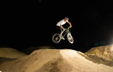 Dirtpark Lingen BMX-Fahrer springt bei Nacht über eine beleuchtete Erdhügelstrecke im Dirtpark Lingen.