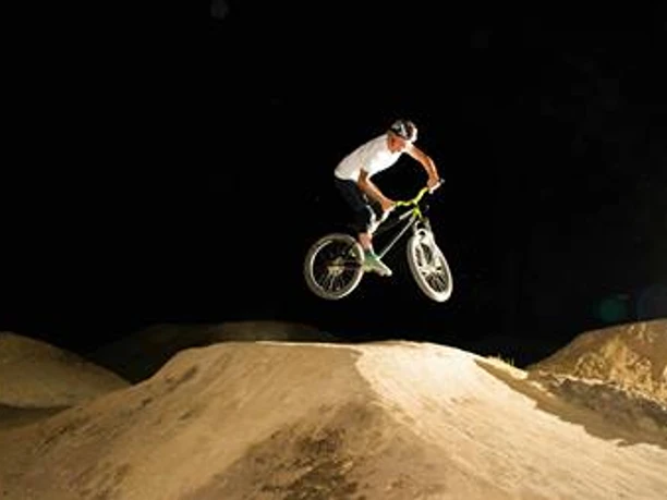 Dirtpark Lingen BMX-Fahrer springt bei Nacht über eine beleuchtete Erdhügelstrecke im Dirtpark Lingen.