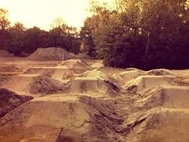 Dirtpark_Lingen_-_Foto_per_Facebook.jpg Sandiger Parcours mit vielen Erdhügeln und Sprungschanzen, umgeben von Bäumen bei Sonnenlicht.