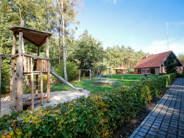 Dorfscheune Varloh Holzspielplatz mit Rutsche und Schaukeln neben einer Scheune mit rotem Dach am Waldrand.