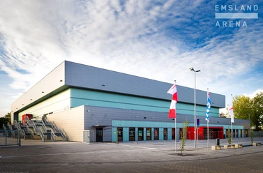 Emsland Arena Lingen Moderne Veranstaltungshalle mit grauer Fassade, breiter Treppe und wehenden Fahnen im Vordergrund.