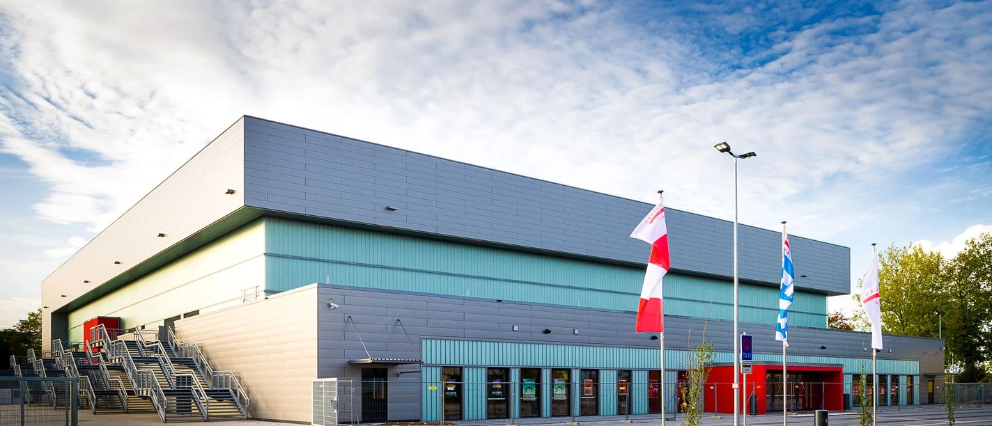 Emsland Arena Lingen Moderne Veranstaltungshalle mit grauer Fassade, breiter Treppe und wehenden Fahnen im Vordergrund.