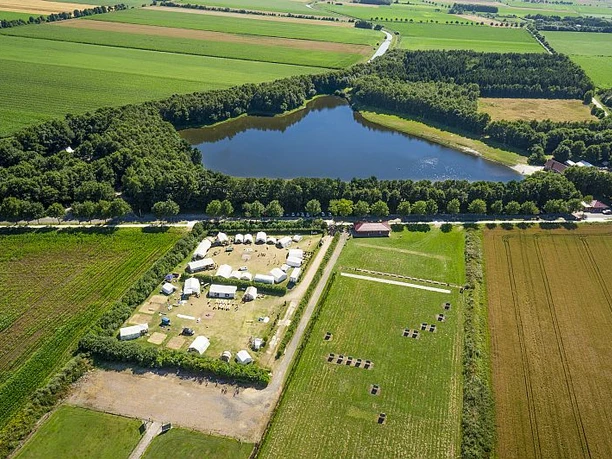 Luftaufnahme eines Sees im Grünen mit angrenzendem Zeltplatz, Feldern und umgebendem Wald.