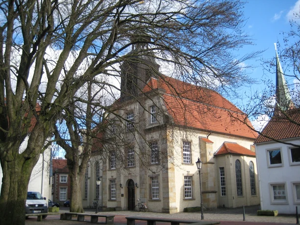 Evangelisch-lutherische Kreuzkirche Barocke Sandsteinkirche mit roten Ziegeldächern und hohem Turm, umgeben von alten Bäumen.
