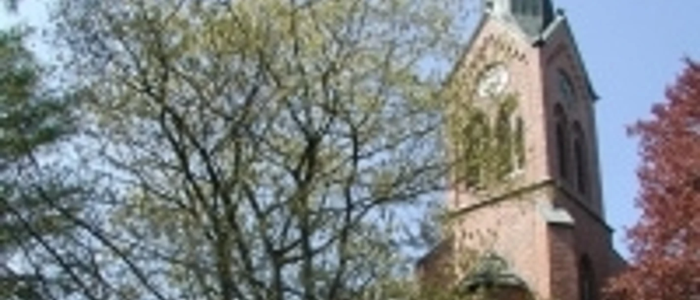 Evangelisch-lutherische Nikolaikirche Rote Backsteinkirche mit hohem Turm und spitzem Dach, umgeben von Bäumen unter blauem Himmel.