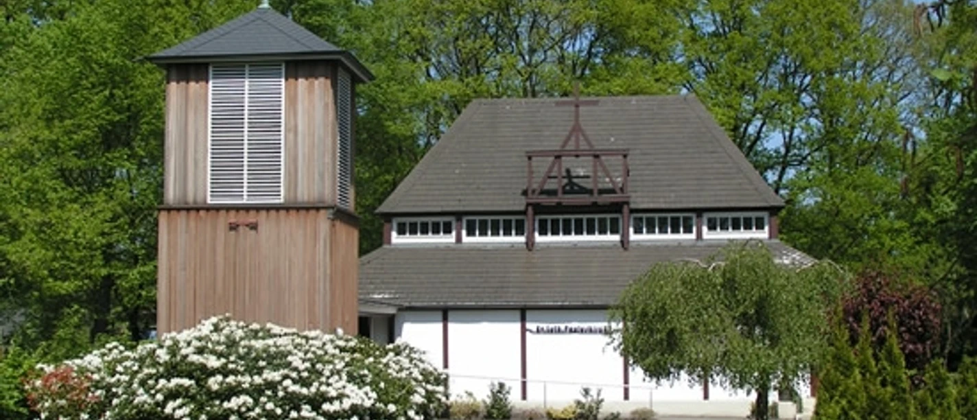 The Evangelical Lutheran Pauluskirche with its freestanding wooden tower, surrounded by greenery and flowers.