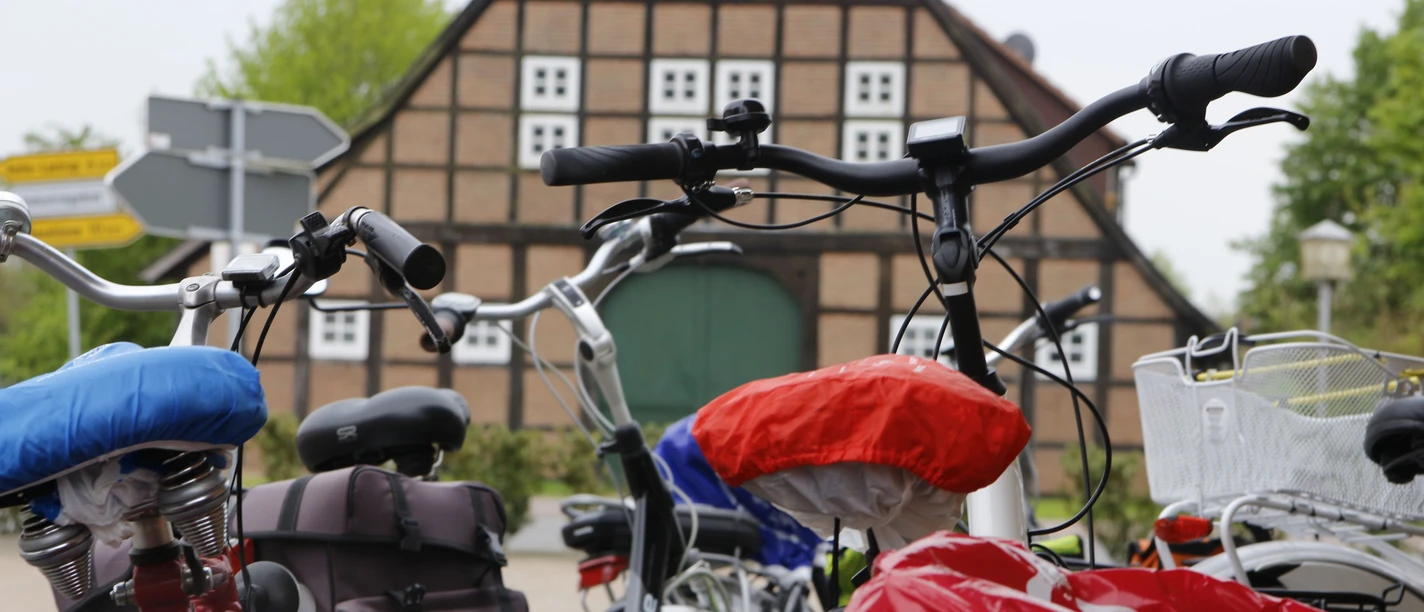 Fahrradverleih Zweirad Wermes Mehrere Fahrräder mit bunten Sattelschonern vor einem traditionellen Fachwerkhaus in Haren.