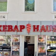 Döner-Restaurant mit auffälligem roten Schild und Glasschiebetür, Werbung für Speisen im Fenster.
