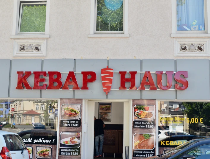 Döner-Restaurant mit auffälligem roten Schild und Glasschiebetür, Werbung für Speisen im Fenster.