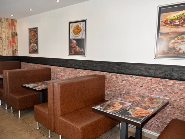 Sitzbereich im Kebap-Haus Moderner Sitzbereich mit braunen Polsterbänken und Tischen; Speisenbilder an den hellen Wänden.
