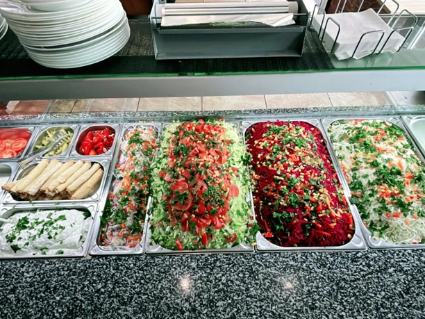 Verschiedene frische Salatzutaten und Soßen in Edelstahlbehältern in einer Selbstbedienungstheke.