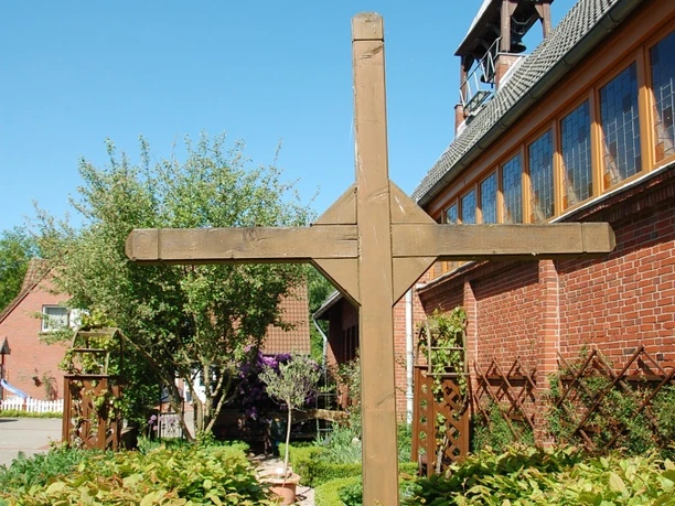 Garten des Nazareners (Bibelgarten) Holzkreuz in gepflegtem Bibelgarten neben roter Backsteinkirche unter klarem blauem Himmel