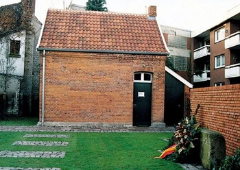 Gedenkort Jüdische Schule Backsteingebäude mit rotem Ziegeldach und Gedenkkranz auf Rasenfläche vor einer Mauer.