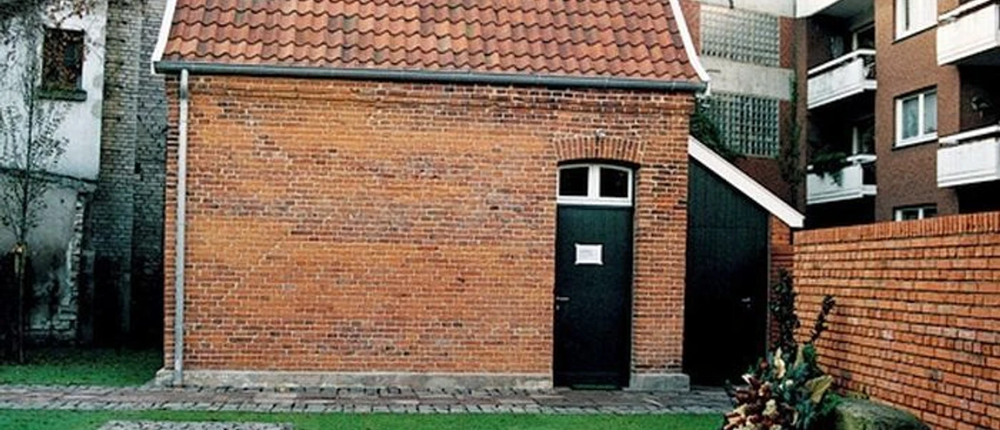 Gedenkort Jüdische Schule Backsteingebäude mit rotem Ziegeldach und Gedenkkranz auf Rasenfläche vor einer Mauer.