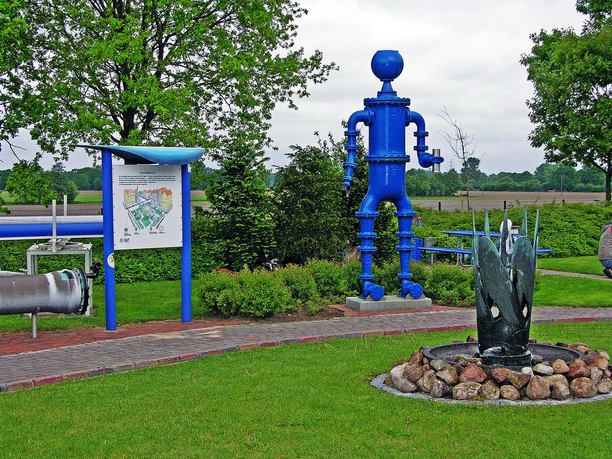 Trinkwasser Erlebnispfad Geeste Blauer Metallmann aus Rohren, Infotafel und kleiner Brunnen auf dem Trinkwasser-Erlebnispfad Geeste.