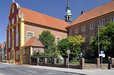 Gymnasialkirche und Residenz Barocke Kirche mit roter Fassade und gelben Zierleisten neben historischem Backsteingebäude in Meppen