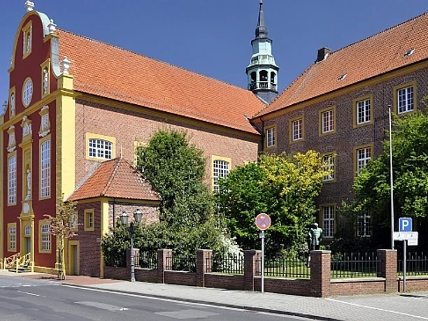 Gymnasialkirche und Residenz Barocke Kirche mit roter Fassade und gelben Zierleisten neben historischem Backsteingebäude in Meppen