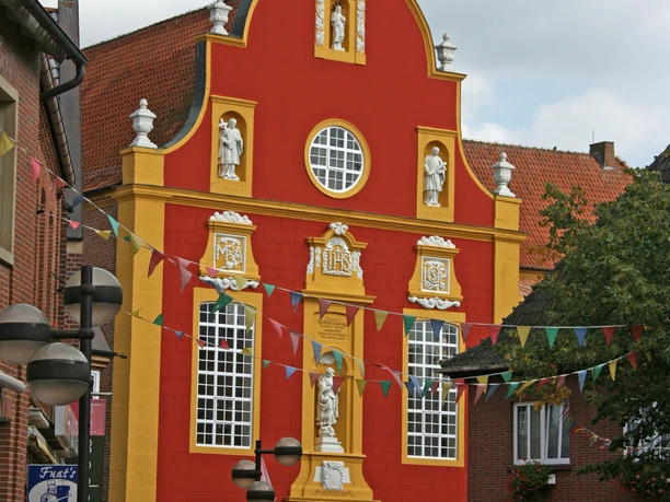 Gymnasialkirche und Residenz Barocke Fassade der Gymnasialkirche in Meppen mit rot-gelbem Putz und weißen Statuenfiguren.