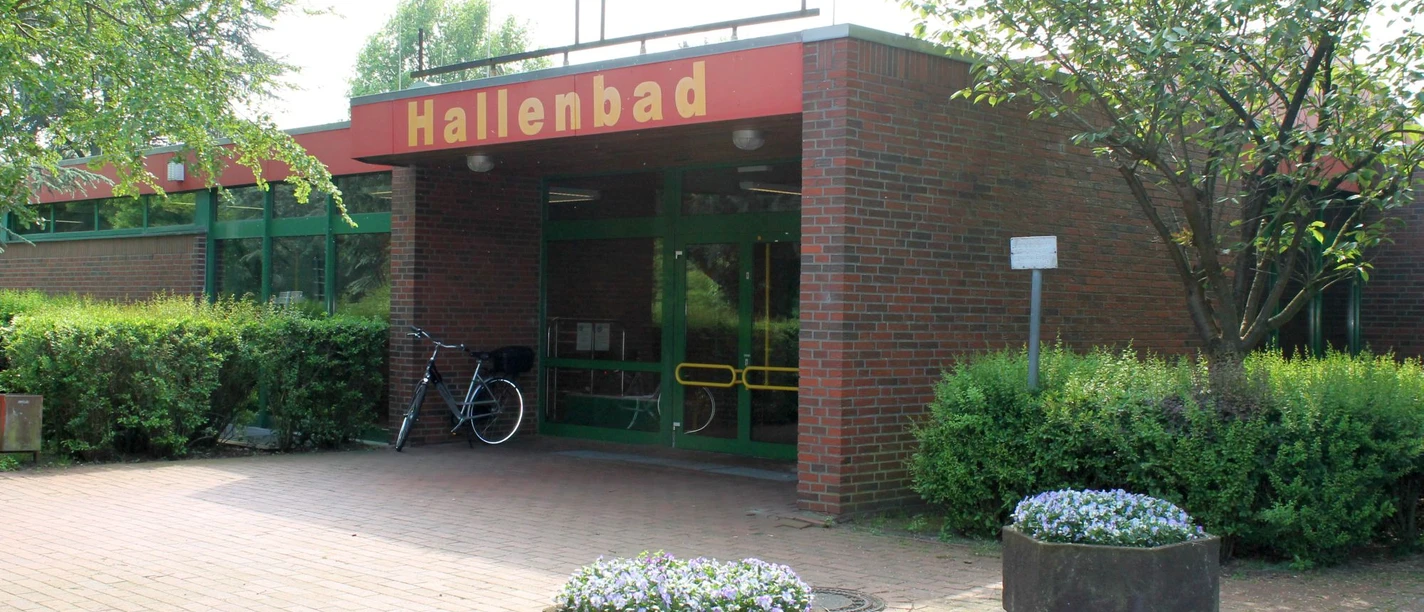 Hallenbad Twist Eingang des Hallenbads Twist mit roter Beschilderung, Backsteinfassade und grüner Glastür.