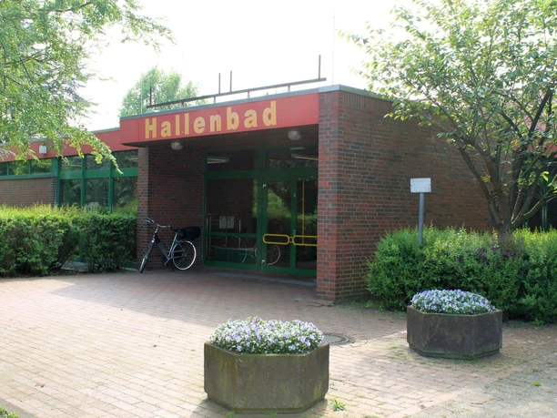 Hallenbad Twist Eingang des Hallenbads Twist mit roter Beschilderung, Backsteinfassade und grüner Glastür.