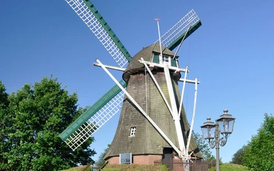 Haren Mersmühle Historische Windmühle in Haren mit grünen Flügeln, rotem Dach und blauem Himmel im Hintergrund.