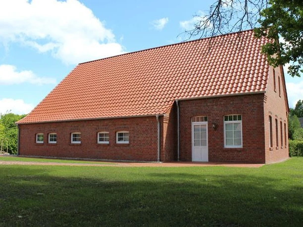 Heimatmuseum Esterwegen Backsteinbau mit rotem Ziegeldach, weißen Fenstern und Türen, umgeben von grüner Wiese und Bäumen.