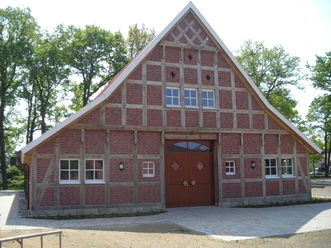 Heimathaus Geeste Traditionelles Fachwerkhaus mit rotem Backstein und großem Holztor vor Bäumen und blauem Himmel