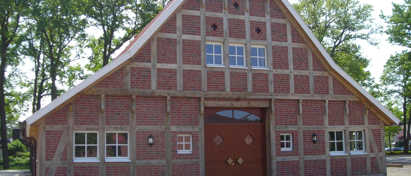 Heimathaus Geeste Traditionelles Fachwerkhaus mit rotem Backstein und großem Holztor vor Bäumen und blauem Himmel