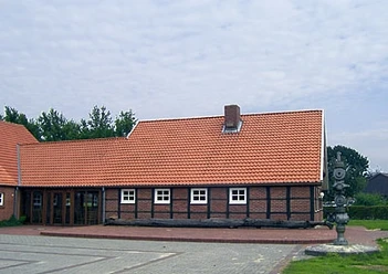 Heimathaus Twist Backsteinhaus mit rotem Ziegeldach, weißen Fenstern und einer Metallskulptur im Vordergrund.