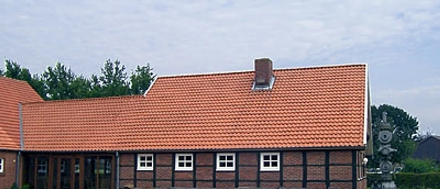 Heimathaus Twist Backsteinhaus mit rotem Ziegeldach, weißen Fenstern und einer Metallskulptur im Vordergrund.