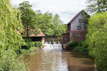Herrenmühle Meppen Historische Wassermühle aus Backstein mit Holzschindeln an einem kleinen Wasserlauf im Grünen.