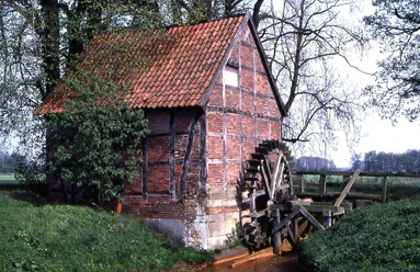 Hesemannsche Wassermühle Historische Fachwerkmühle mit hölzernem Wasserrad an einem kleinen Bach, umgeben von Bäumen.
