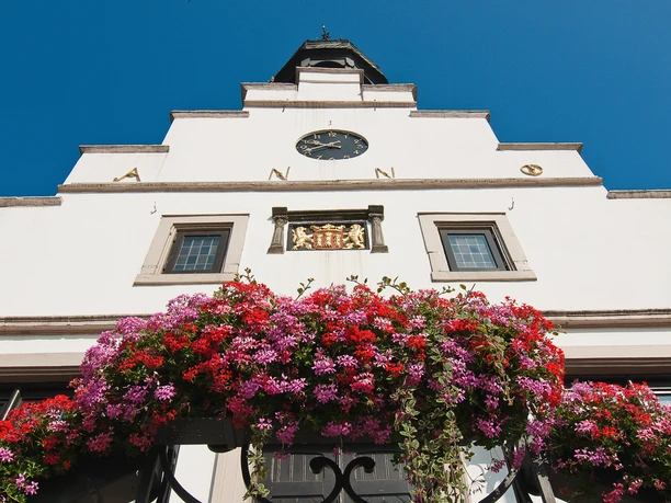 Historisches Rathaus Lingen Fassade des historischen Rathauses Lingen mit Ziergiebel, Uhr und Blumenschmuck unter blauem Himmel.