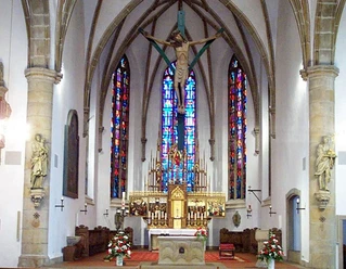 St.-Vincentius-Kirche Innenraum der St.-Vincentius-Kirche mit Altar, Kreuzigungsgruppe und farbigen Glasfenstern.