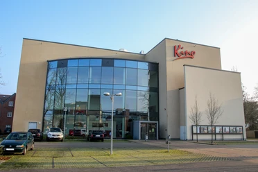 Kino Papenburg Modernes Kinohaus mit großer Glasfassade, rotem Schriftzug und kleinem Parkplatz im Vordergrund.
