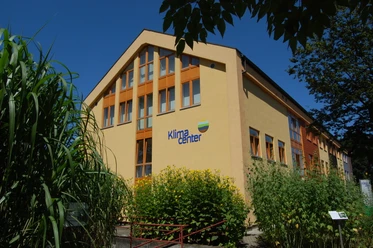Klimacenter Werlte Modernes Gebäude des Klimacenters Werlte mit gelber Fassade, großen Fenstern und grüner Bepflanzung.