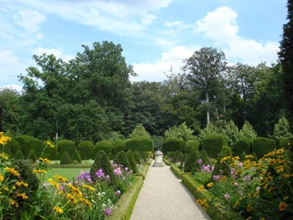 Klostergarten Clemenswerth Symmetrischer Gartenweg mit blühenden Stauden, exakt geschnittenen Hecken und einer Statue am Ende.