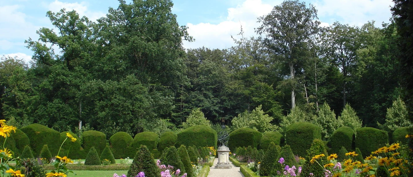 Klostergarten Clemenswerth Symmetrischer Gartenweg mit blühenden Stauden, exakt geschnittenen Hecken und einer Statue am Ende.