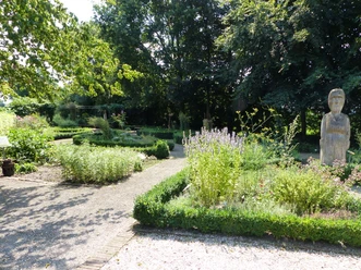 Kräutergarten an der Mersmühle Kräuterbeete mit blühenden Pflanzen und Holzfigur im grünen Garten an der historischen Mersmühle.