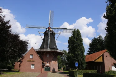Kreutzmanns Mühle Historische Windmühle mit rotem Backsteinsockel und Holzflügeln vor blauem Himmel in Werlte.